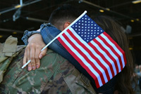 Woman holding a U.S. flag hugging an american soldier.