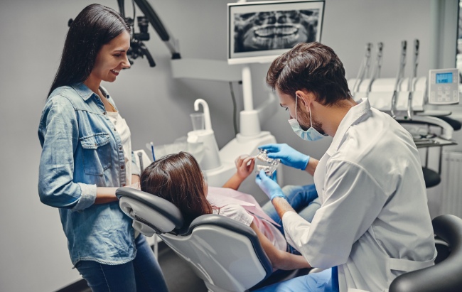 Girl in dentist chair with mom standing by