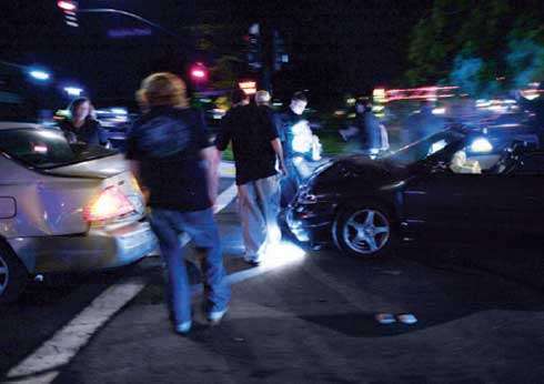photo of nighttime car crash with teens walking around