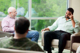 Photo shows three men seated in a circle and engaged in a serious discussion.
