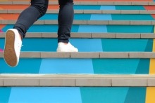 Lower part of teenage girl in casual shoe walking up outdoor colorful stair.
