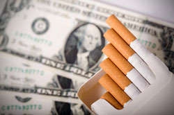 An open package of cigarettes rests on top of some dollar bills.